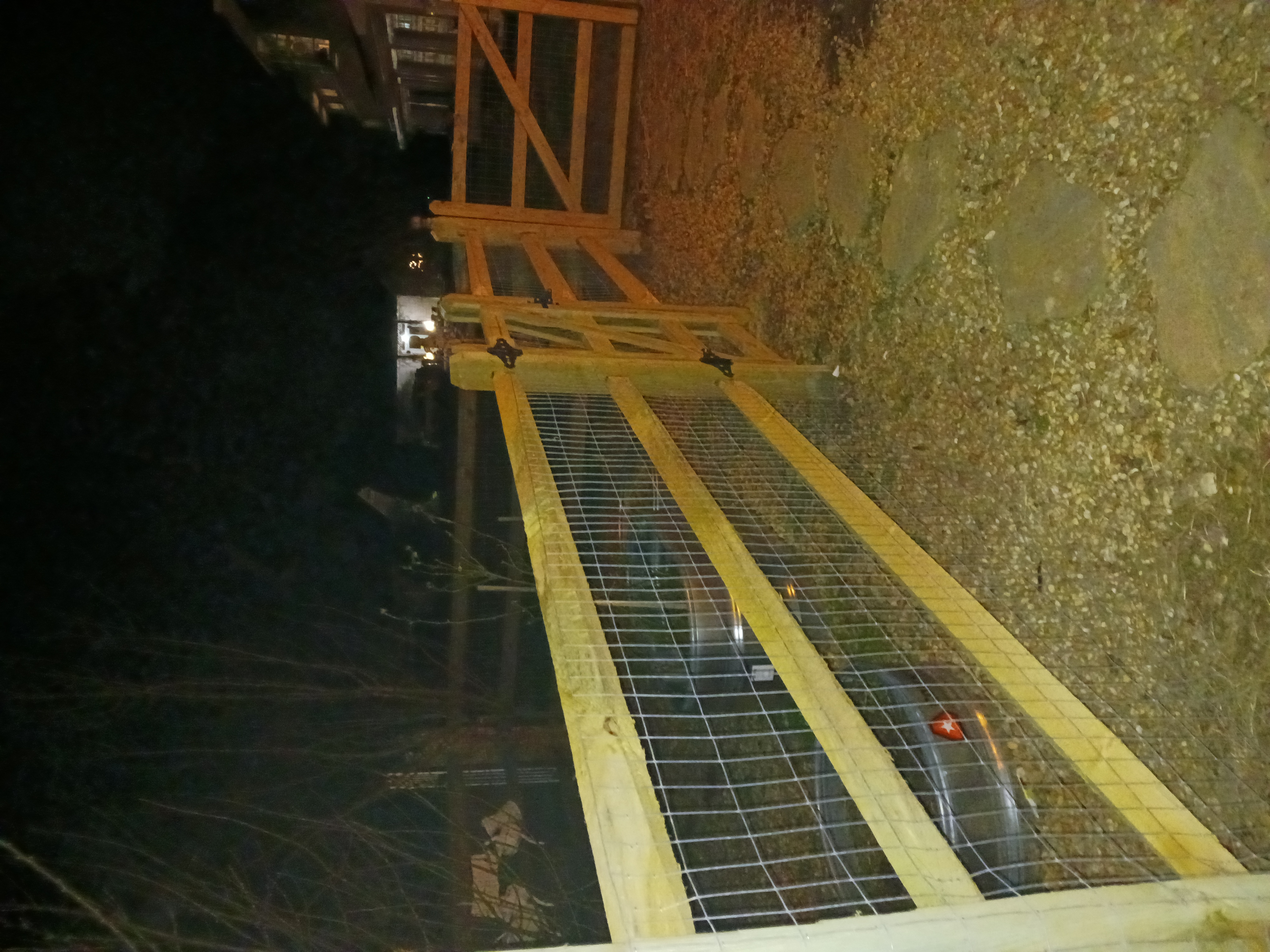 Wood and wire farm-style fence and gate at night near a driveway.